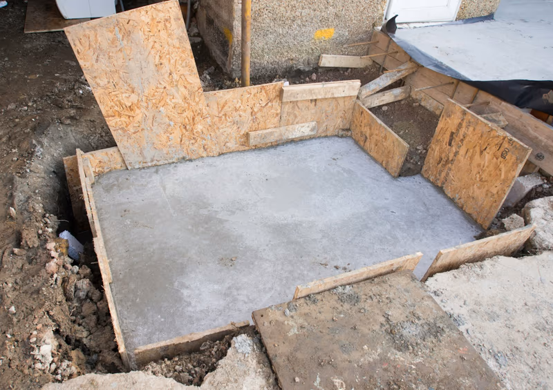 A newly poured concrete footing pad in an excavation with timber formwork still in place