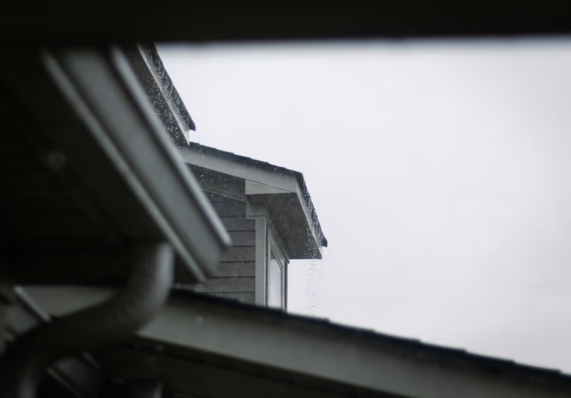 Rain running off a roof edge and gutter during a storm, seen from beneath an eave